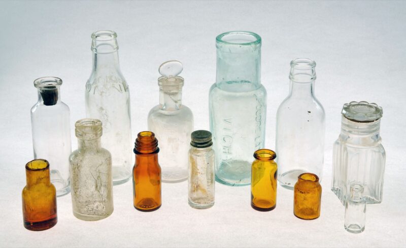 Échantillon de la production de la verrerie normande de Tourouvre au début du 20e s. : flacons et fioles de verre blanc, bleuté ou jaune, dont un petit flacon pour la poudre Vichy, montrant la place croissante des verres à usage médico-pharmaceutique dans l'industrie verrière du début du 20e siècle en France